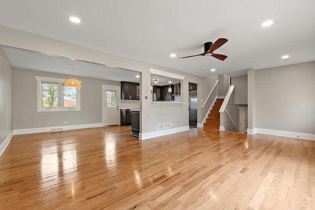 unfurnished living room featuring baseboards, visible vents, stairway, and light wood-style floors