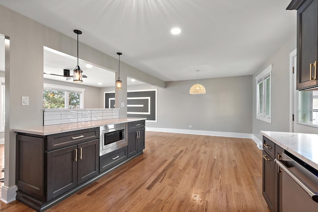 kitchen featuring baseboards, light wood-style flooring, appliances with stainless steel finishes, and decorative light fixtures