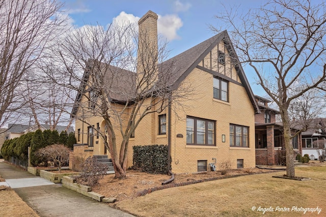 view of side of property with a lawn, brick siding, a chimney, and roof with shingles