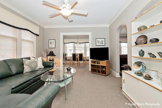 living area featuring arched walkways, ceiling fan, ornamental molding, and light carpet