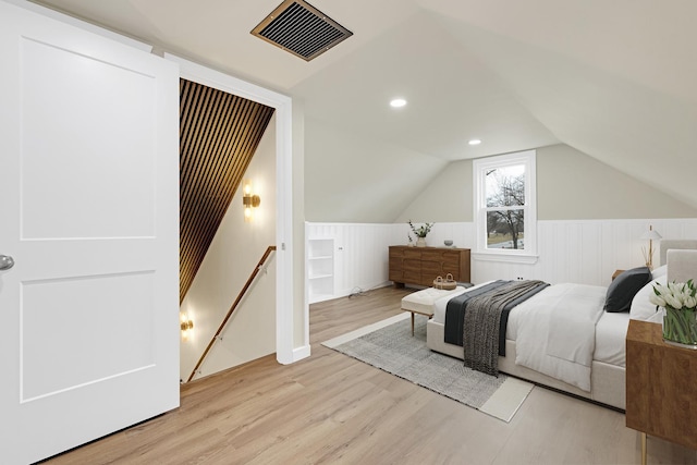 bedroom featuring visible vents, a wainscoted wall, vaulted ceiling, and light wood-type flooring