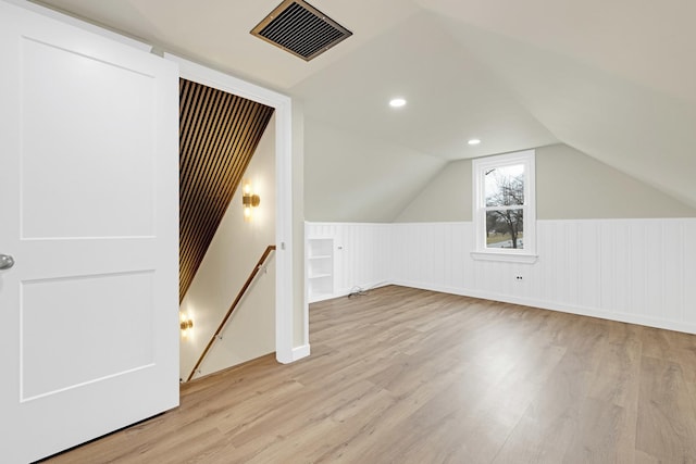additional living space with visible vents, wood finished floors, vaulted ceiling, and a wainscoted wall