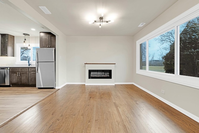 unfurnished living room featuring light wood-type flooring, baseboards, a glass covered fireplace, and visible vents