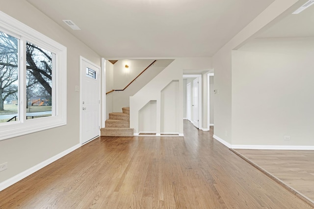 unfurnished living room with baseboards, visible vents, wood finished floors, and stairway
