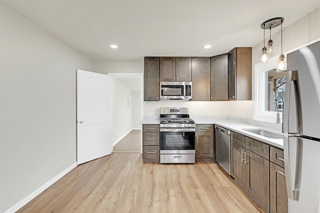 kitchen featuring dark brown cabinetry, appliances with stainless steel finishes, a sink, light wood-style floors, and light countertops