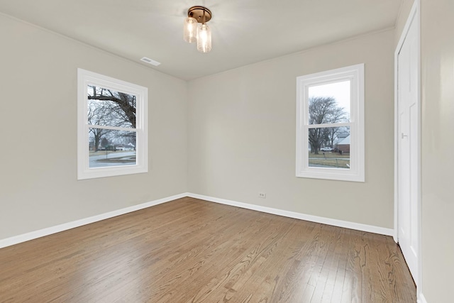 spare room with baseboards, visible vents, and wood finished floors