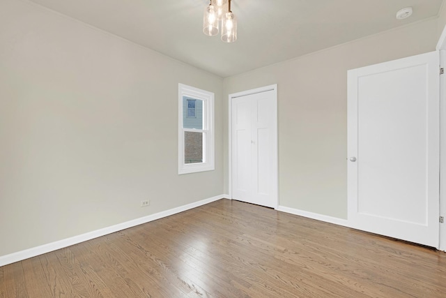 unfurnished bedroom with baseboards, an inviting chandelier, wood finished floors, and a closet