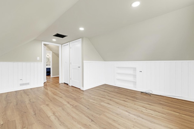 additional living space featuring visible vents, wainscoting, lofted ceiling, built in shelves, and light wood-style flooring