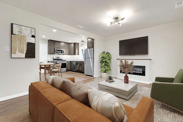 living area with a glass covered fireplace, light wood-style flooring, recessed lighting, baseboards, and visible vents