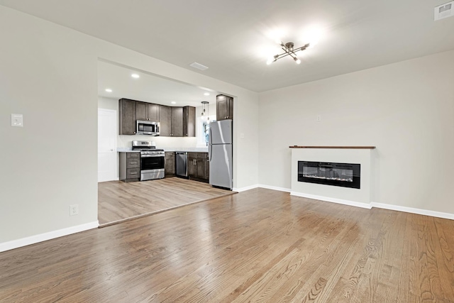 unfurnished living room featuring visible vents, a glass covered fireplace, baseboards, recessed lighting, and light wood-style flooring