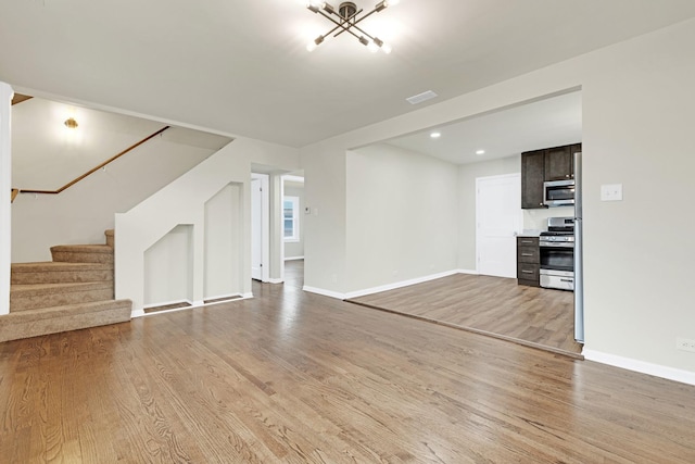 unfurnished living room with stairs, light wood-style floors, baseboards, recessed lighting, and a chandelier