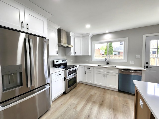 kitchen featuring a sink, light countertops, white cabinets, stainless steel appliances, and wall chimney exhaust hood