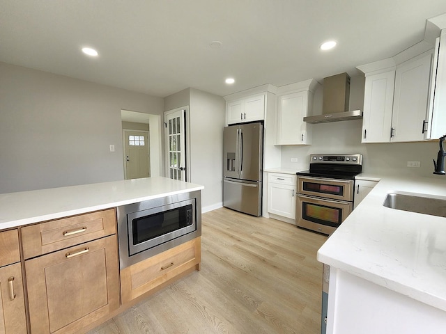 kitchen with light wood-style floors, wall chimney range hood, recessed lighting, a sink, and appliances with stainless steel finishes