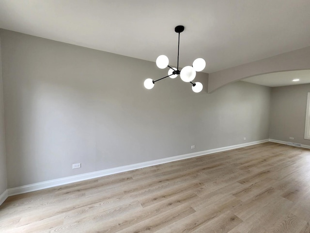 empty room with arched walkways, baseboards, a chandelier, and light wood-style flooring