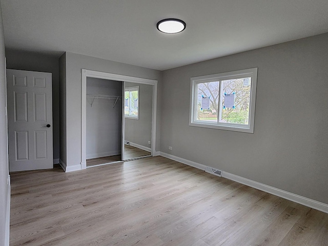 unfurnished bedroom with visible vents, light wood-style flooring, baseboards, and a closet