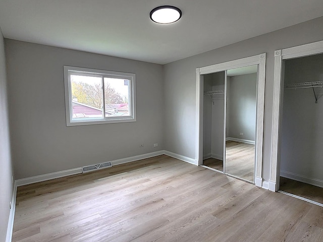 unfurnished bedroom with visible vents, baseboards, light wood-style flooring, and two closets