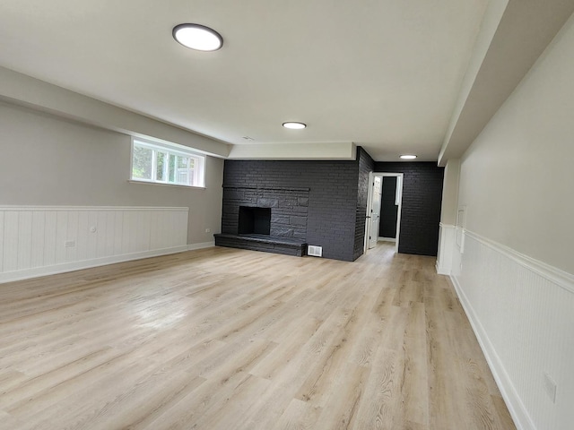 unfurnished living room featuring wainscoting, visible vents, a stone fireplace, and light wood finished floors