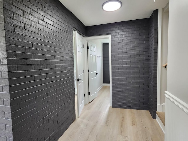 hallway with light wood-style flooring and brick wall