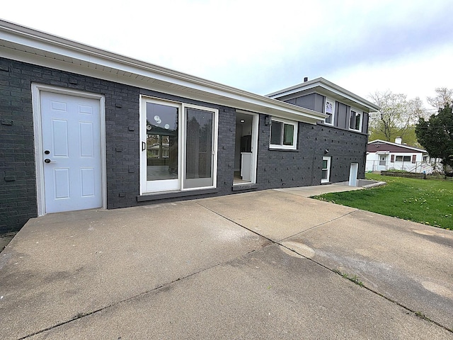 exterior space with a lawn, a patio area, and brick siding