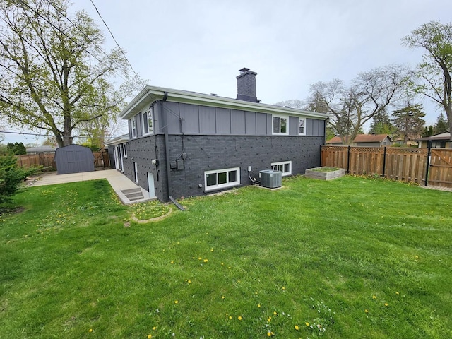 back of property featuring a fenced backyard, a chimney, a yard, and a shed