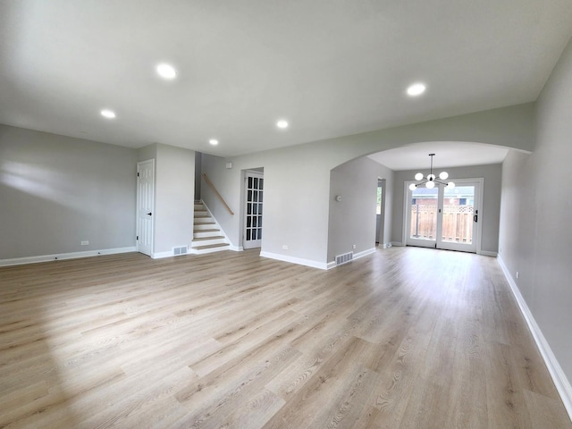 unfurnished living room featuring arched walkways, baseboards, a notable chandelier, and visible vents