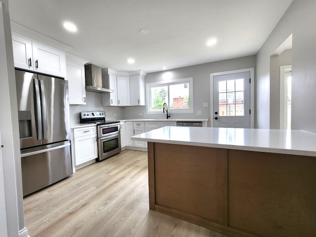 kitchen with appliances with stainless steel finishes, wall chimney exhaust hood, a sink, light countertops, and light wood-style flooring