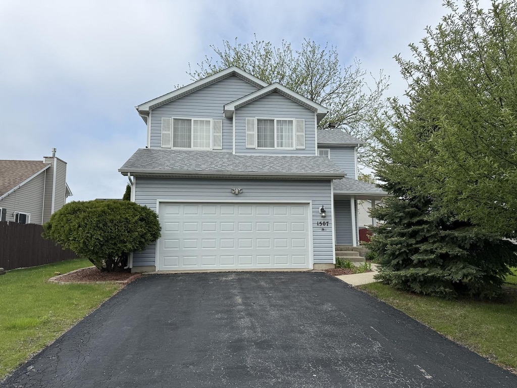 traditional-style home featuring fence, an attached garage, roof with shingles, and aphalt driveway