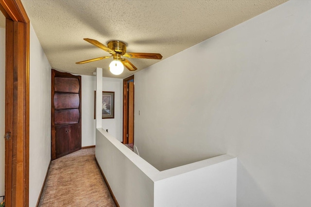 corridor featuring light colored carpet, a textured ceiling, baseboards, and an upstairs landing