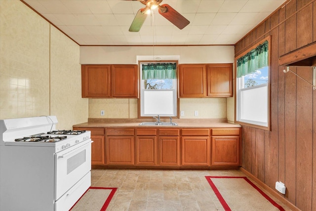 kitchen featuring a sink, white range with gas stovetop, brown cabinets, and a healthy amount of sunlight