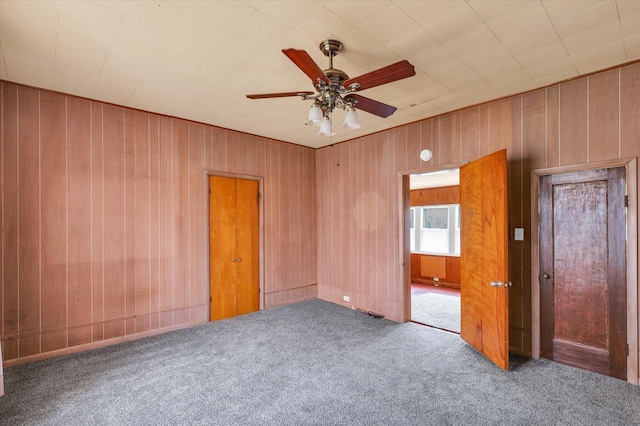 carpeted spare room with wooden walls and a ceiling fan