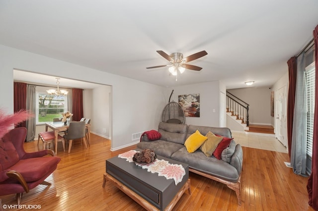 living area with visible vents, stairs, baseboards, light wood-style flooring, and ceiling fan with notable chandelier