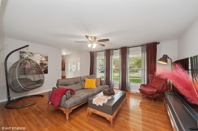 living room featuring baseboards, a ceiling fan, and light wood finished floors