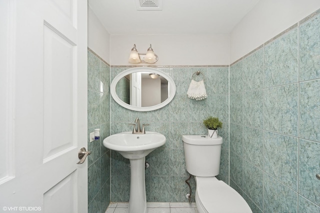 half bath featuring visible vents, tile patterned floors, toilet, and tile walls