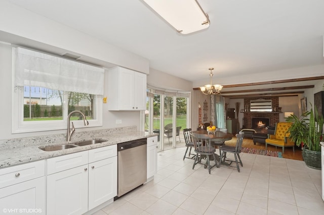 kitchen with stainless steel dishwasher, a brick fireplace, plenty of natural light, a chandelier, and a sink