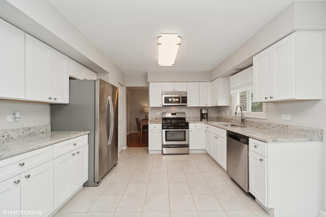 kitchen featuring white cabinets, light stone counters, a sink, stainless steel appliances, and light tile patterned floors