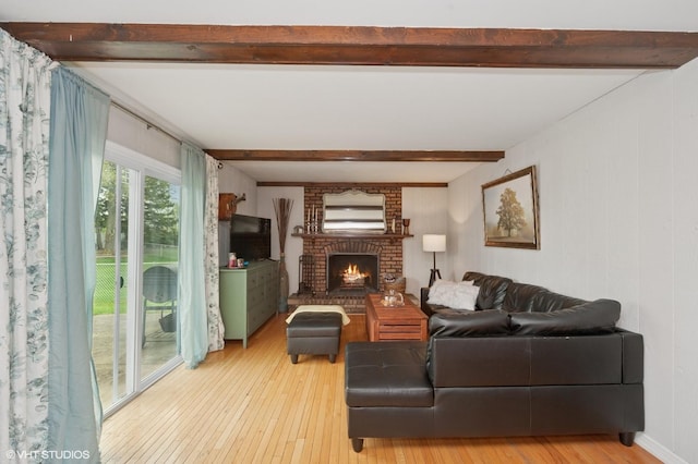living room featuring a brick fireplace, beamed ceiling, and light wood-style flooring
