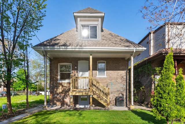 view of front facade with a front lawn, central AC, brick siding, and roof with shingles