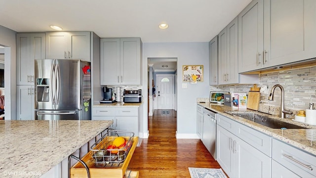 kitchen with appliances with stainless steel finishes, a sink, gray cabinetry, dark wood-style flooring, and light stone countertops