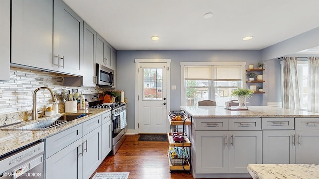 kitchen featuring stainless steel appliances, a sink, gray cabinets, dark wood-type flooring, and decorative backsplash