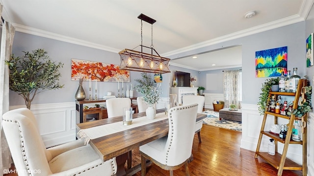 dining room featuring ornamental molding, wainscoting, wood finished floors, a decorative wall, and recessed lighting