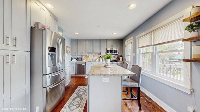 kitchen with appliances with stainless steel finishes, dark wood finished floors, a kitchen island, a breakfast bar area, and baseboards