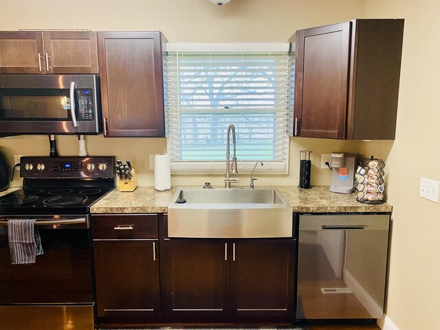kitchen with light countertops, dark brown cabinets, appliances with stainless steel finishes, and a sink