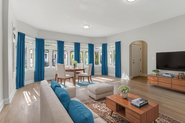 living area featuring arched walkways, baseboards, and light wood-type flooring