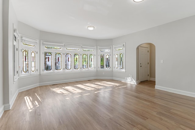 empty room with arched walkways, light wood-type flooring, and baseboards