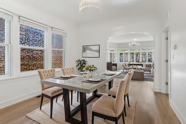 dining space featuring arched walkways, wood finished floors, a chandelier, and baseboards