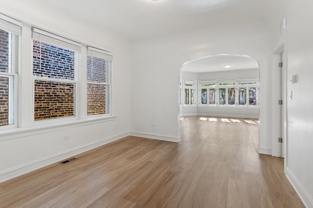 empty room featuring wood finished floors, arched walkways, and baseboards