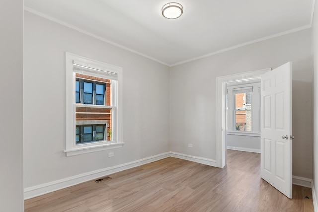 empty room with ornamental molding, light wood-style floors, and baseboards