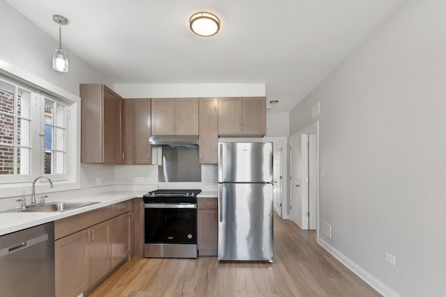 kitchen with appliances with stainless steel finishes, a sink, light wood-type flooring, and under cabinet range hood