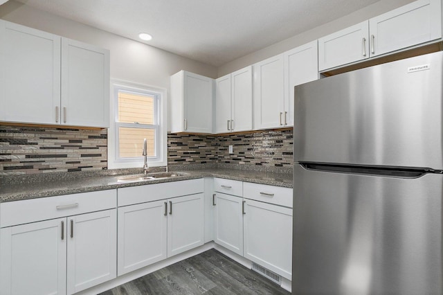 kitchen featuring dark countertops, a sink, freestanding refrigerator, white cabinetry, and dark wood-type flooring