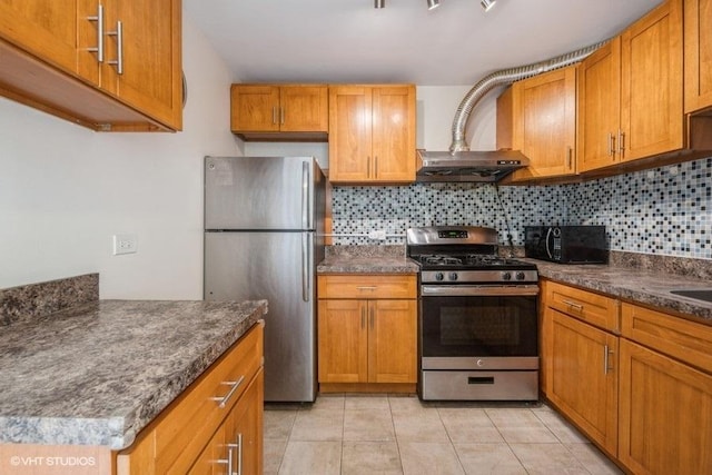 kitchen with wall chimney range hood, decorative backsplash, appliances with stainless steel finishes, brown cabinets, and light tile patterned floors